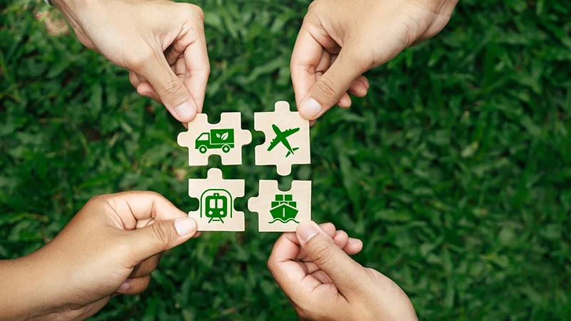 Hands assembling puzzle pieces with green sustainability icons on grass