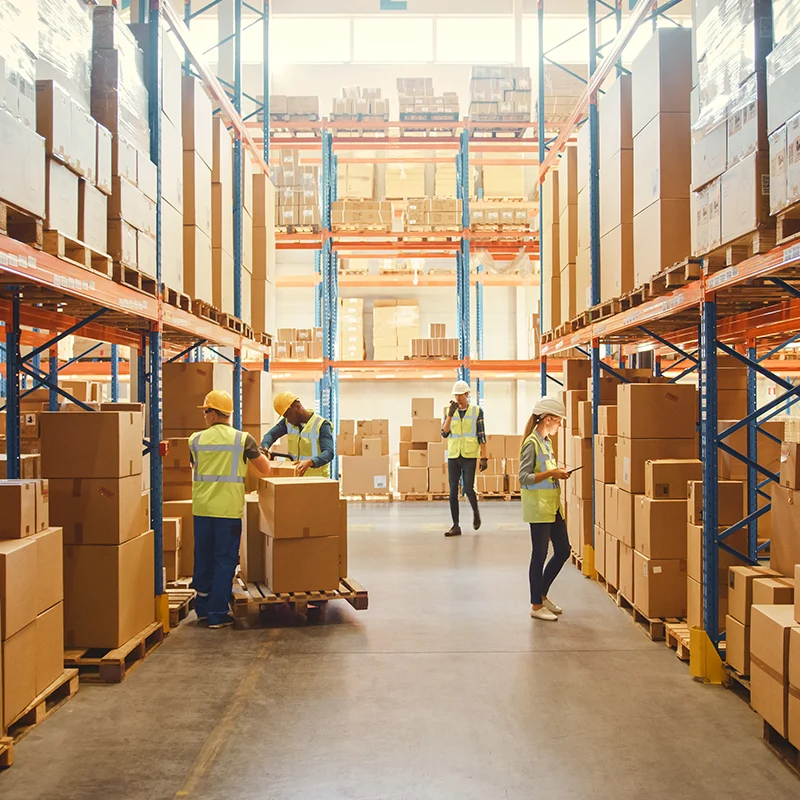 Workers inside a large modern warehouse with tall shelves of goods